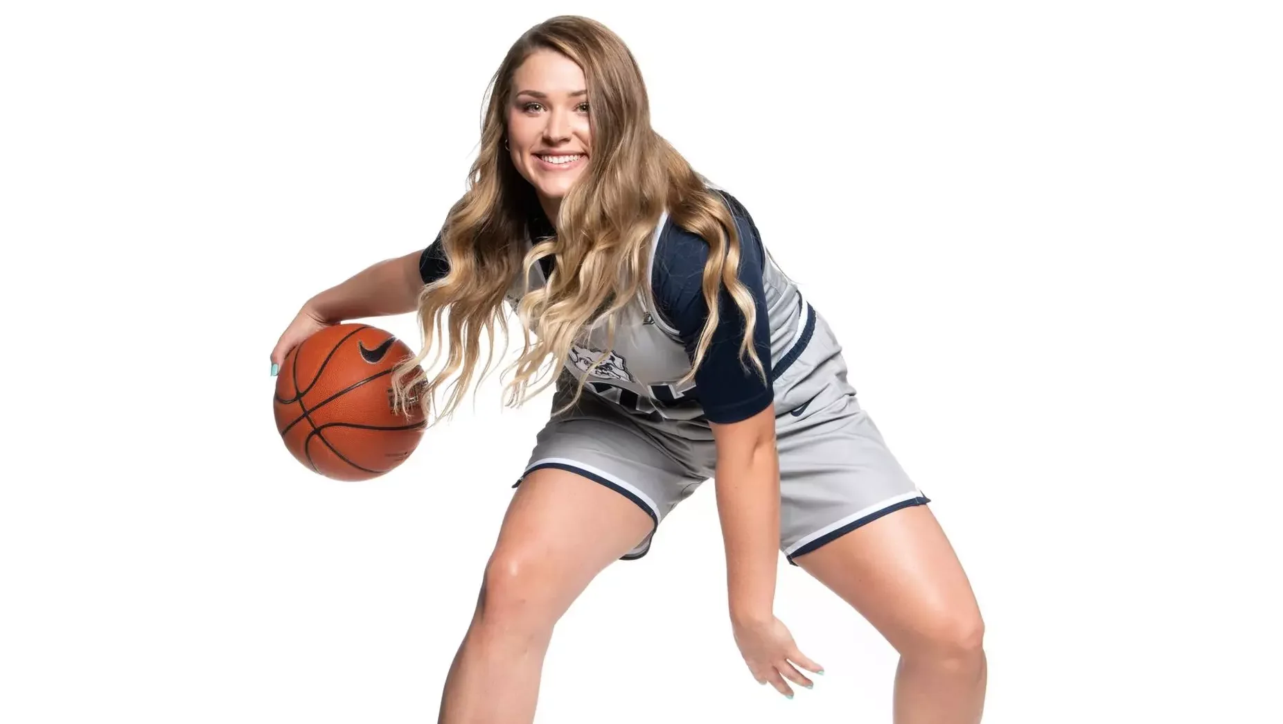 Young woman in a basketball uniform holding a basketball, posing against a white background.