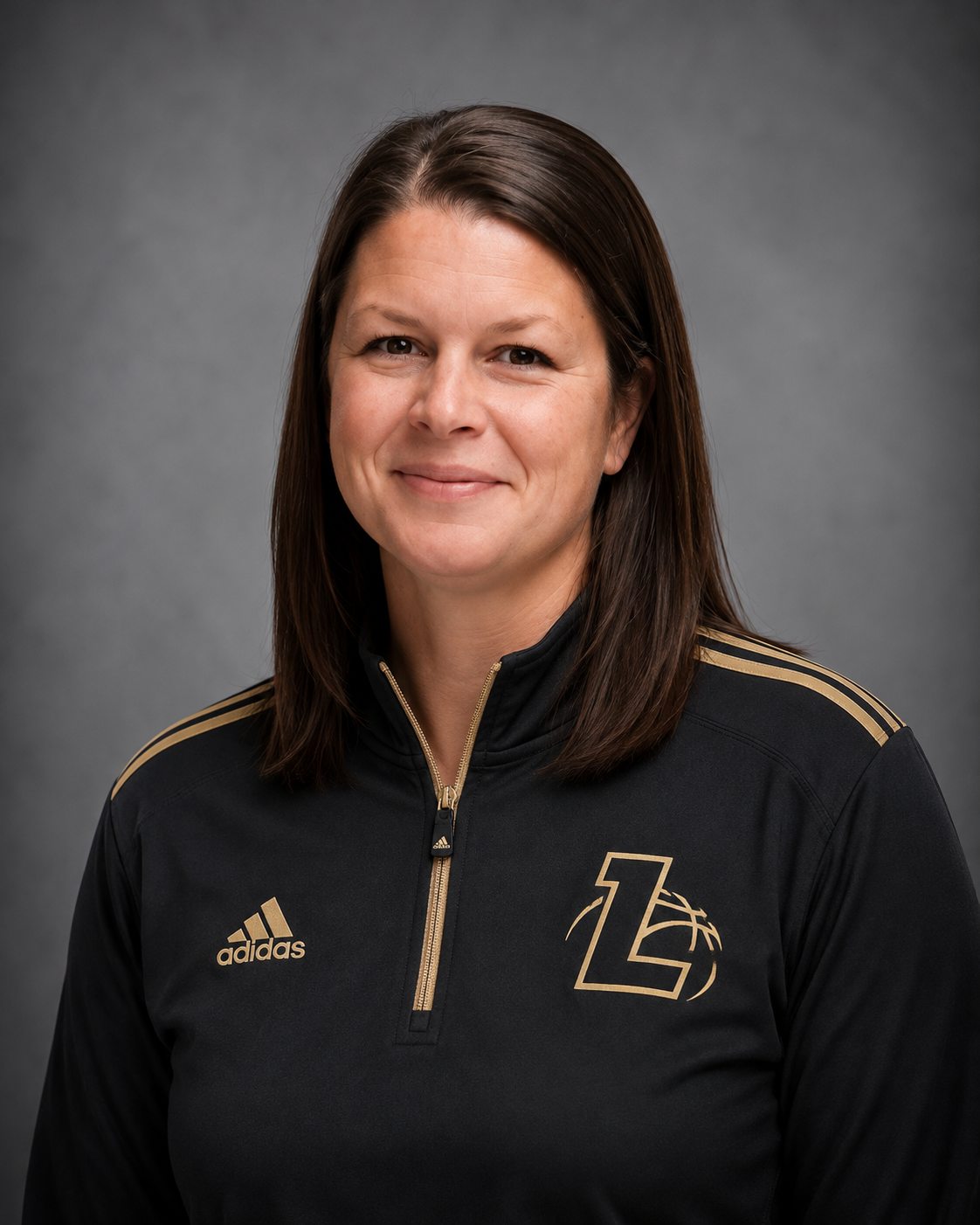 A woman with shoulder-length brown hair smiling, wearing a black Adidas sports jacket with gold accents and a logo on the left side.
