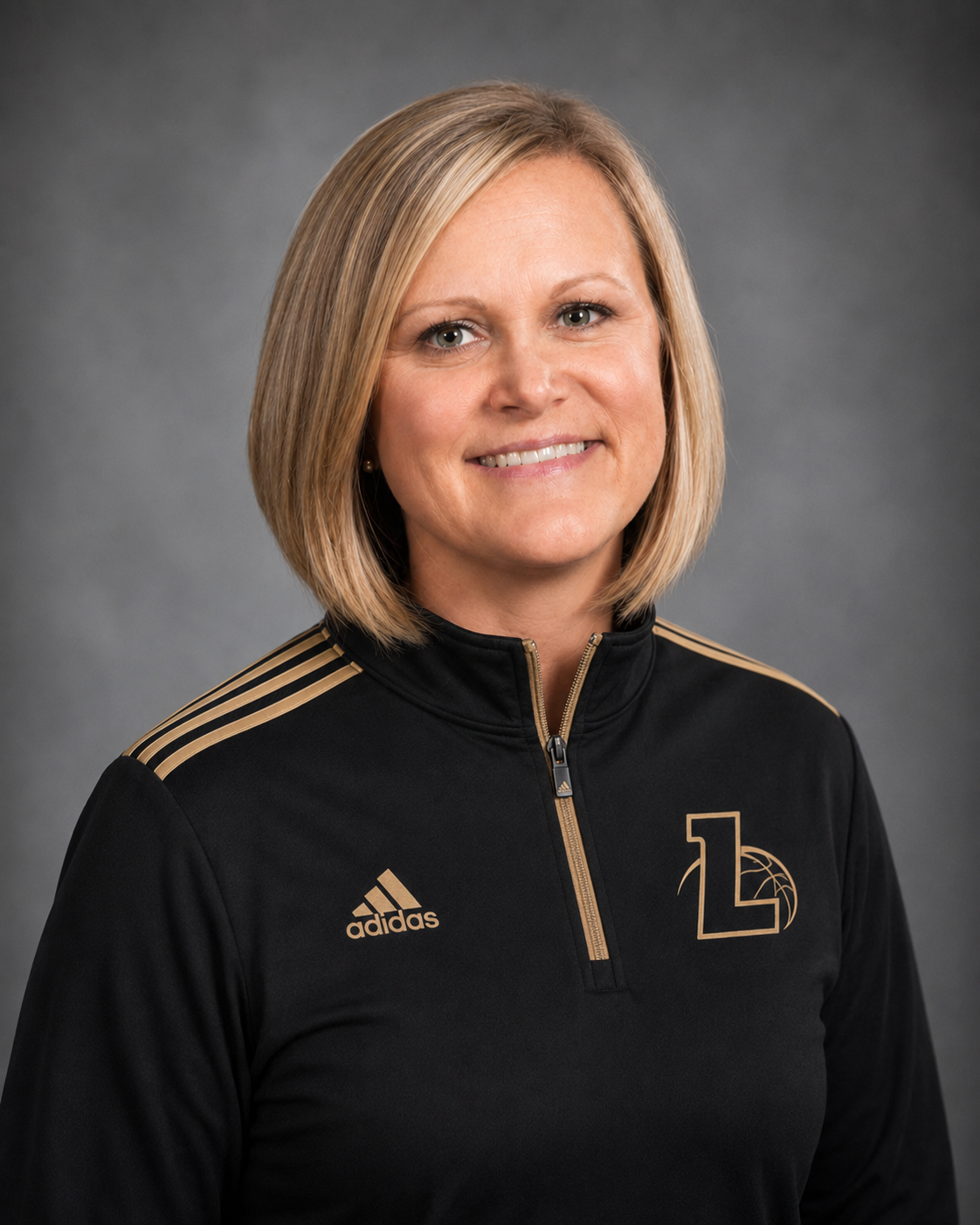 A woman with short blonde hair smiling, wearing a black Adidas athletic jacket with gold accents and a logo on the chest.