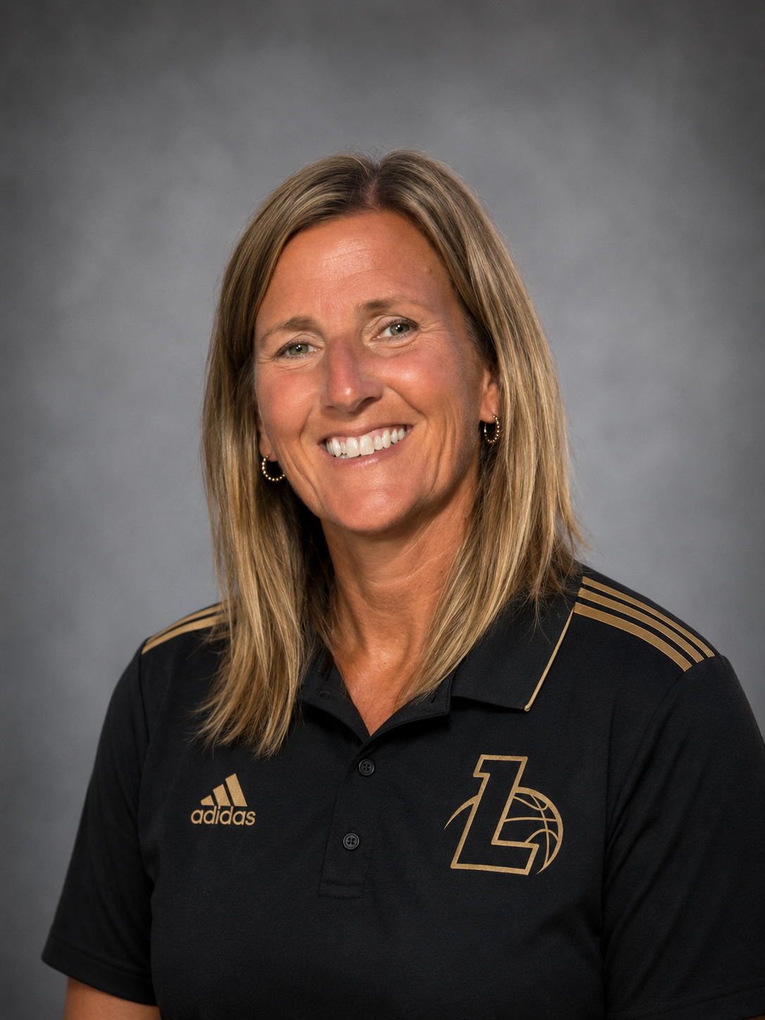 A woman in a black Adidas polo shirt with gold accents and logo, smiling against a gray background.
