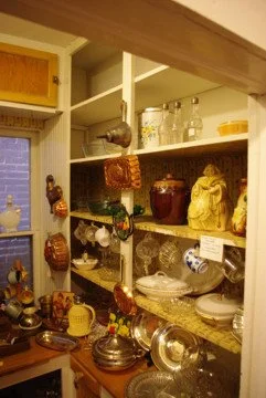 A kitchen with open shelves filled with various dishes, jars, and decorative items, and a countertop with metal and ceramic cookware.