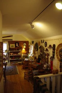 Interior of a cozy room decorated with vintage and rustic furniture, wall decorations, and various decorative items on shelves and walls.