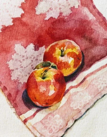 Watercolor painting of two red apples with green leaves on a pink and white patterned fabric background.