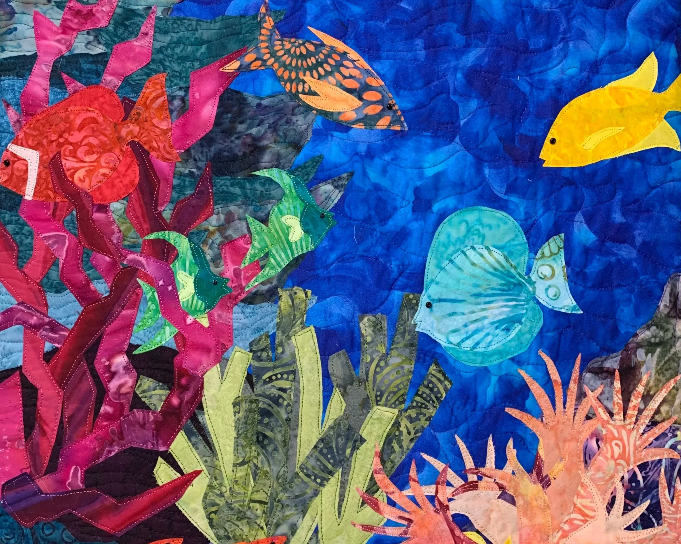 A colorful quilt with various fish and underwater seaweed designs, featuring bright colors such as pink, orange, yellow, green, and blue.