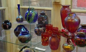 Collection of colorful glass vases and jars displayed on a glass shelf.