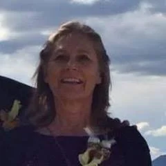 Woman smiling outdoors with a cloudy sky in the background.