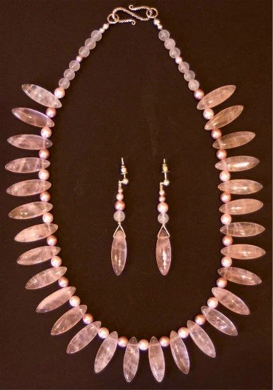 Pink and clear beaded necklace with matching earrings displayed on a black surface.