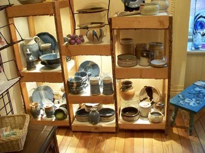 Wooden shelves with pottery and dishes in a room with wooden floor and blue furniture.