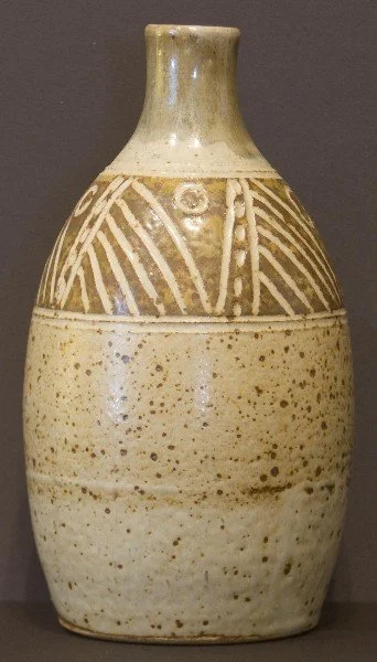 A ceramic vase with a narrow neck and rounded body, featuring beige and cream colors with decorative carved geometric patterns near the top.