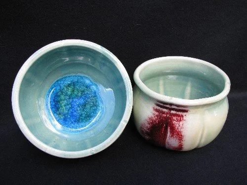 Two ceramic bowls placed on a black surface, one with a blue interior and the other with a white exterior and red streaks.