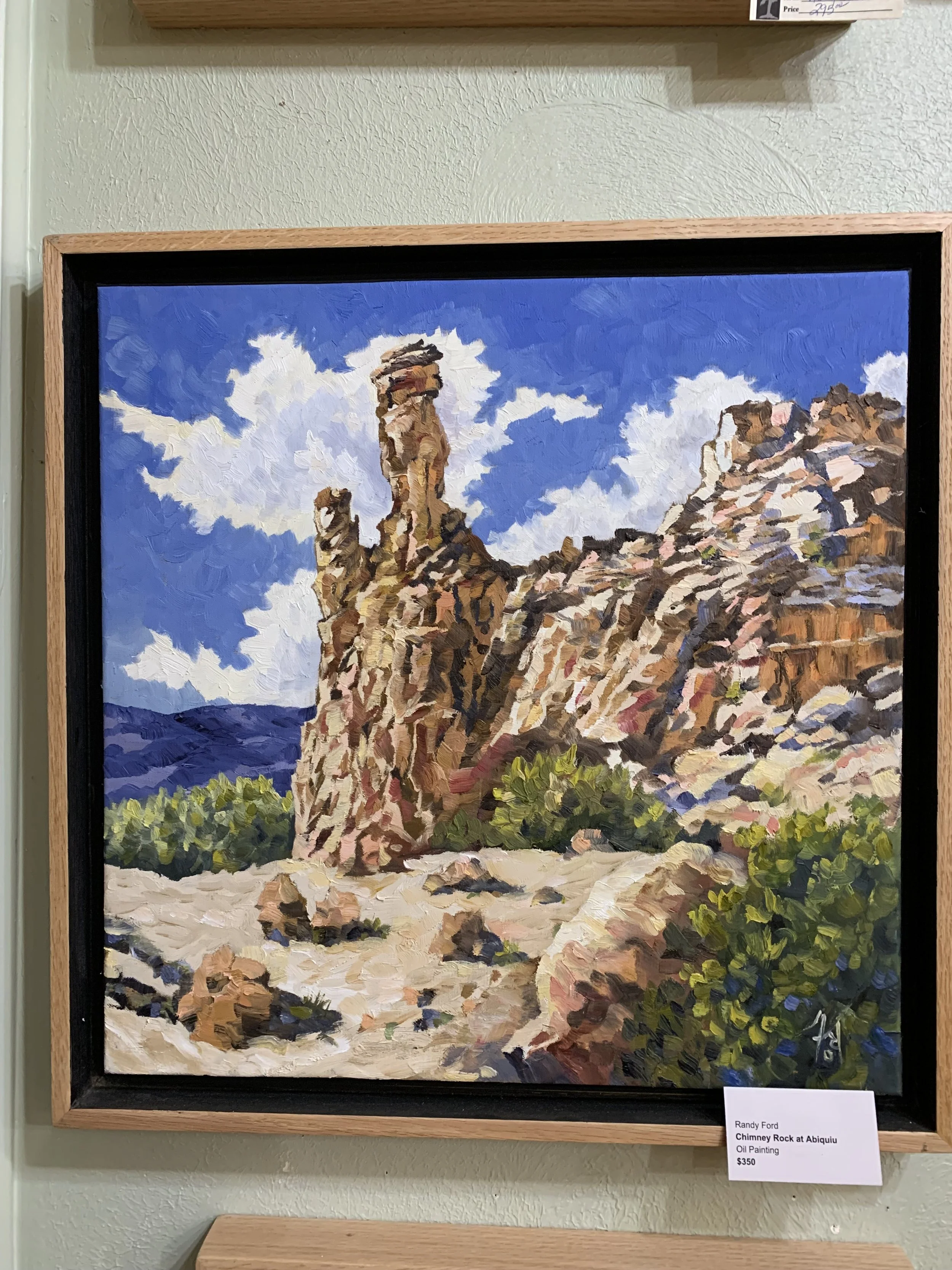 Oil painting of a chimney rock formation at Abiquiu, with blue sky and white clouds in the background, signed by Randy Ford. Frame visible, price tag reads $350.