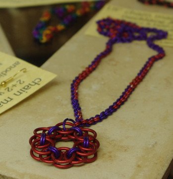 Colorful beaded necklace with a large red and purple floral pendant resting on a beige surface.