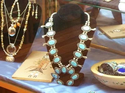 Display of jewelry including necklaces and earrings on a jewelry stand and table, with a bowl of decorative stones and a book.