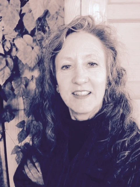 A woman with long, curly hair standing indoors near a wall with plants.