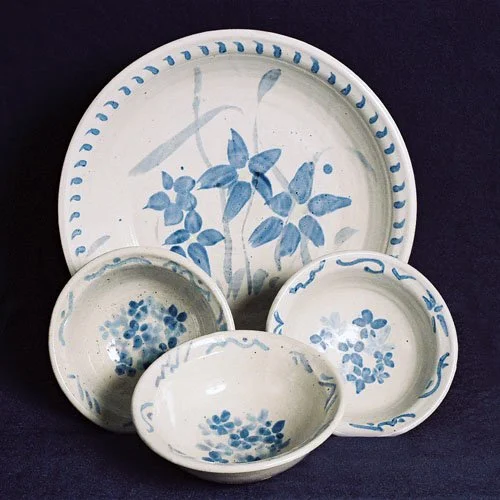 Set of five white ceramic bowls with blue floral and leaf patterns, stacked or arranged on a dark surface.