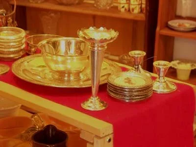 A display of gold and silver tableware including plates, bowls, and goblets on a red tablecloth, with some pieces stacked.