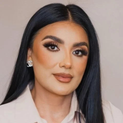 Portrait of a woman with long black hair, makeup, and earrings wearing a beige blazer.
