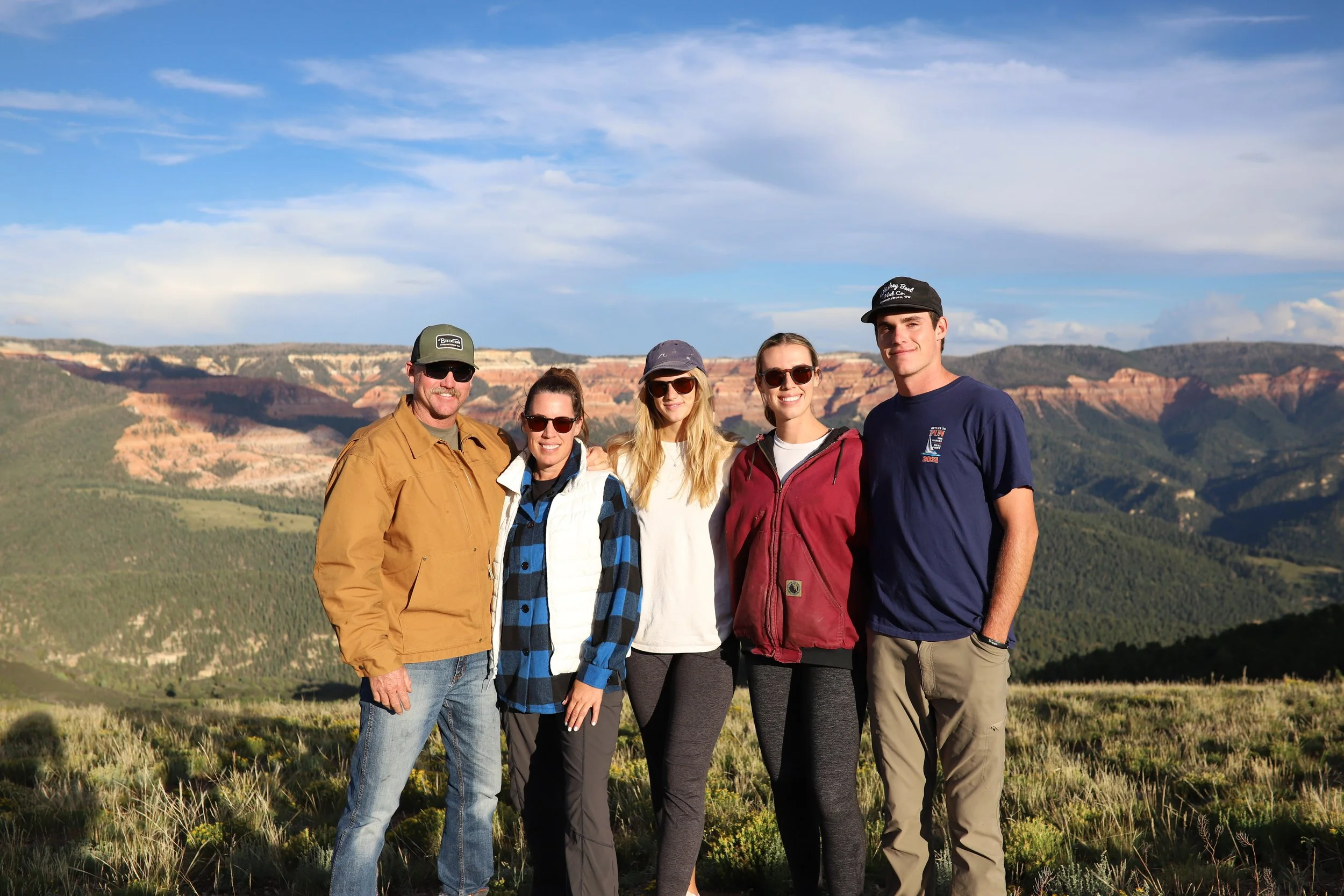 Group of five people standing outdoors in front of colorful canyon landscape.