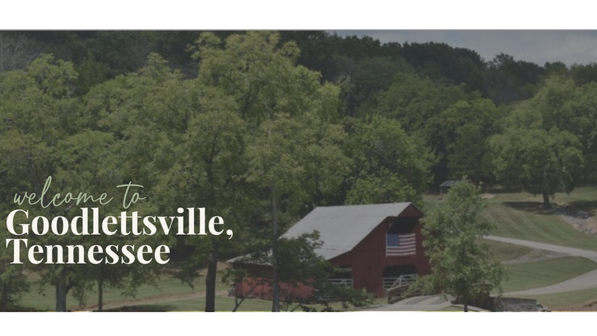 A rustic red barn with a flag hanging outside, surrounded by green trees and grassy fields in Goodlettsville, Tennessee.