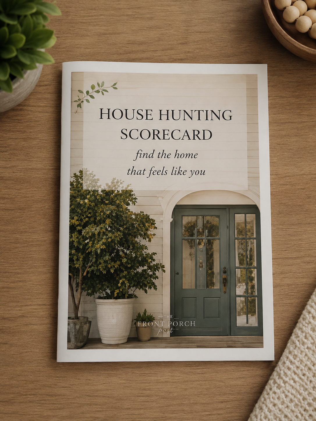 House hunting scorecard on a wooden table surrounded by a potted plant, a bowl of white soybeans, and a knitted cloth.