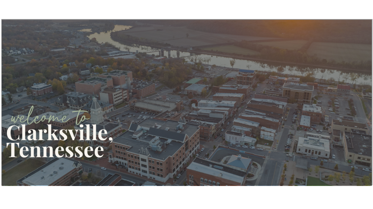 Aerial view of Clarksville, Tennessee cityscape with downtown buildings, streets, parking lots, and a river in the background at sunset.