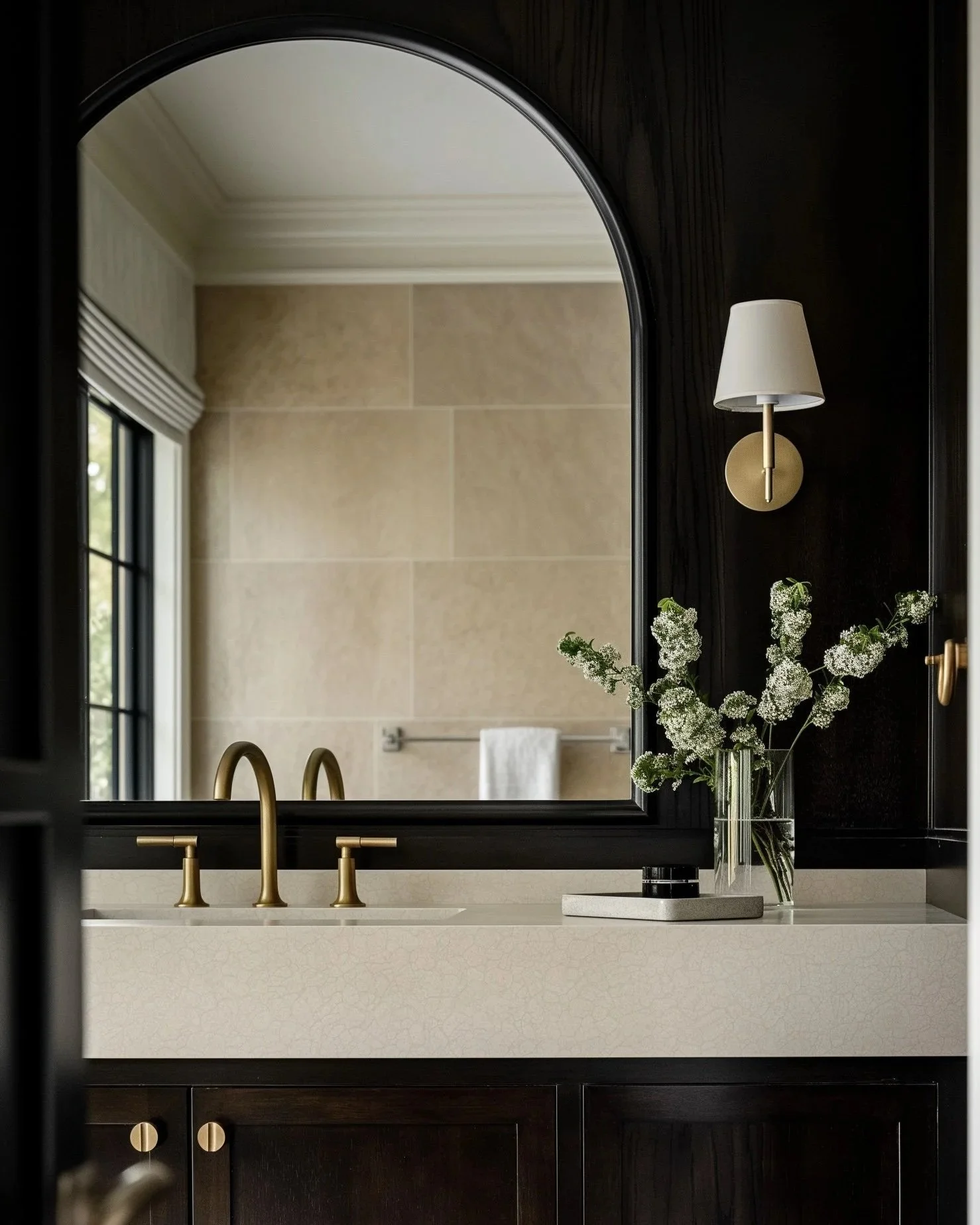 Refined bathroom with warm stone, dark wood cabinetry, brass fixtures and classic architectural details, representing Riley Baker Interiors’ Charleston interior design and finish selection services.