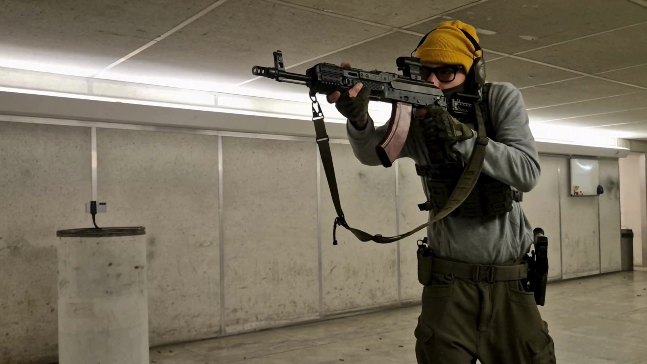 Person in tactical gear aiming a rifle in an indoor shooting range.