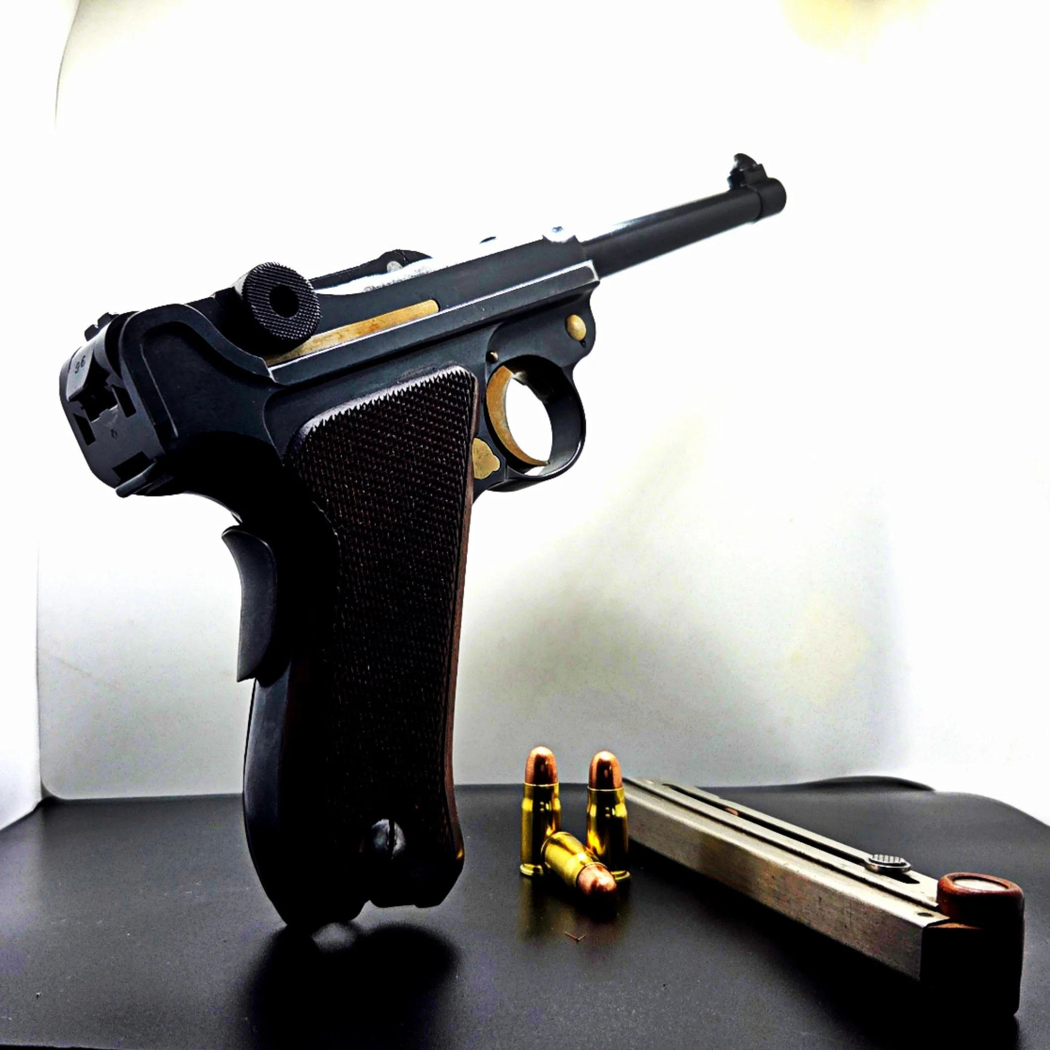 A semi-automatic pistol with a black frame and barrel, along with two golden bullets and a small red object, placed on a gray surface with a background of white and yellow.