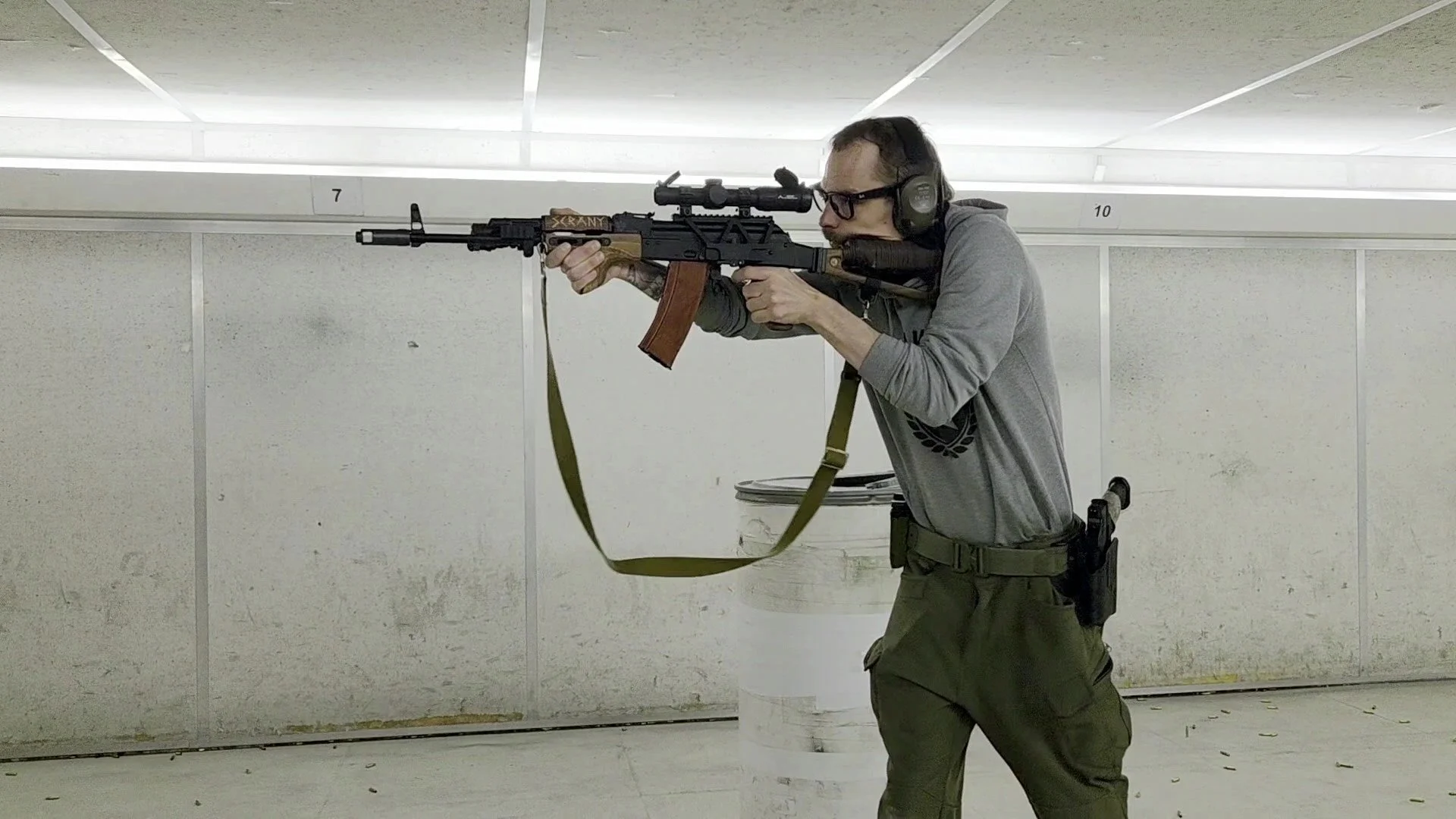 A man at an indoor shooting range aiming a rifle.