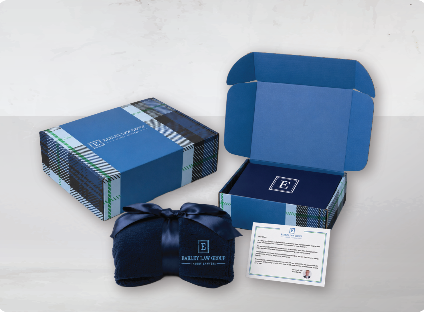 Open blue and plaid patterned box labeled 'Earley Law Group' with a navy blue blanket with 'Earley Law Group' embroidered on it, and a note or letter from Earley Law Group.