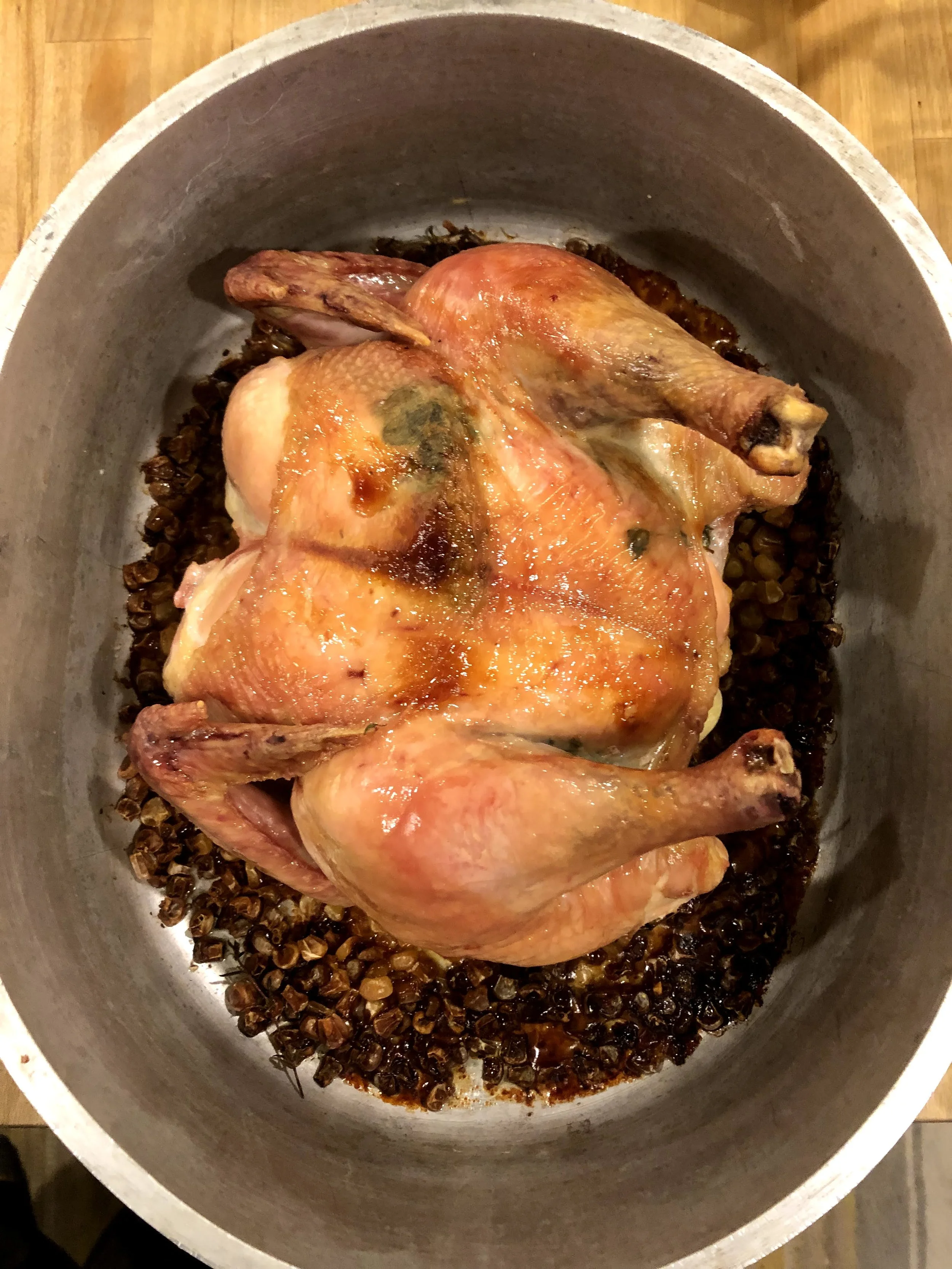 Raw whole chicken in a roasting pan with seasoned lentils underneath, ready for cooking.