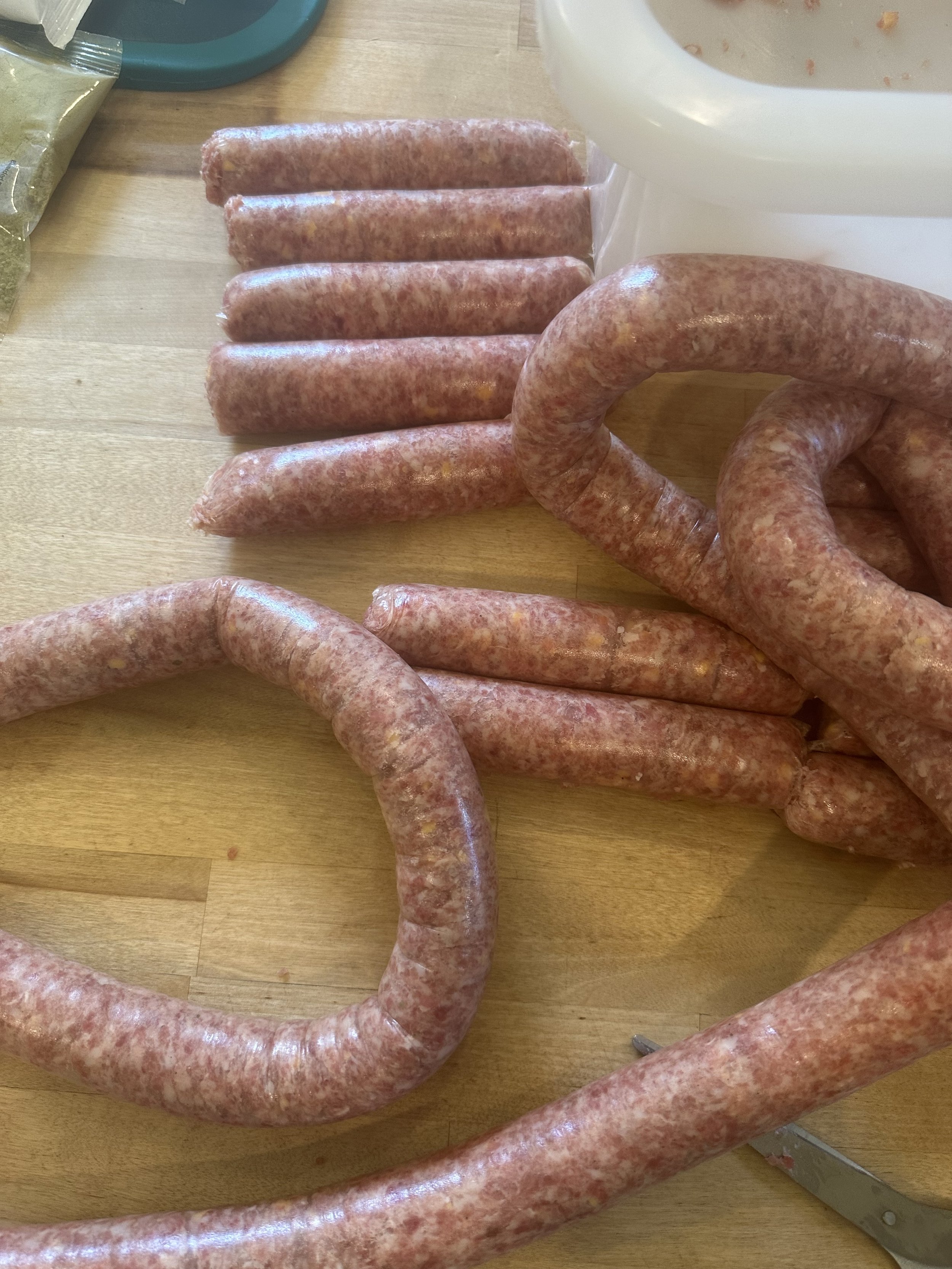 Raw sausages on a wooden surface with a knife and a meat grinder in the background.
