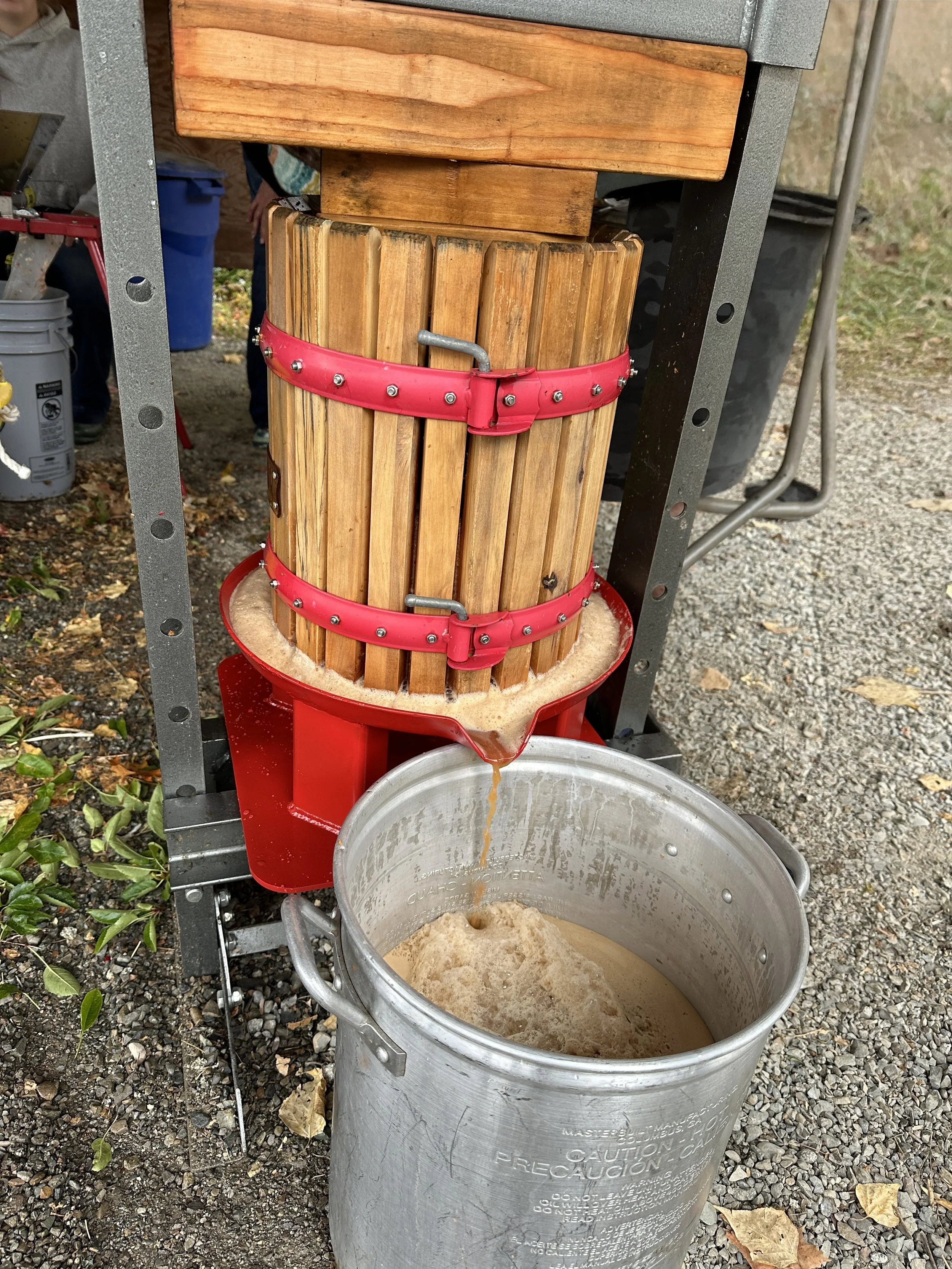 A cider press with a wooden barrel and a metal barrel below it, used for extracting juice from apples or other fruits.