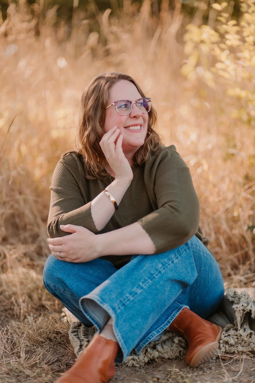 Ashley Sullivan, a licensed therapist, seated in a field of tall grass, smiling gently