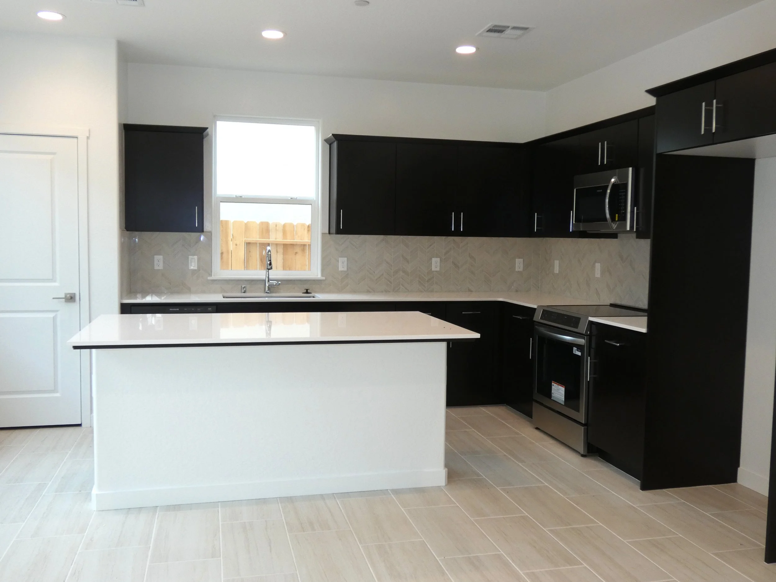 Modern kitchen with white granite coutertops, separate island, stainless steel appliances, and recessed lighting.