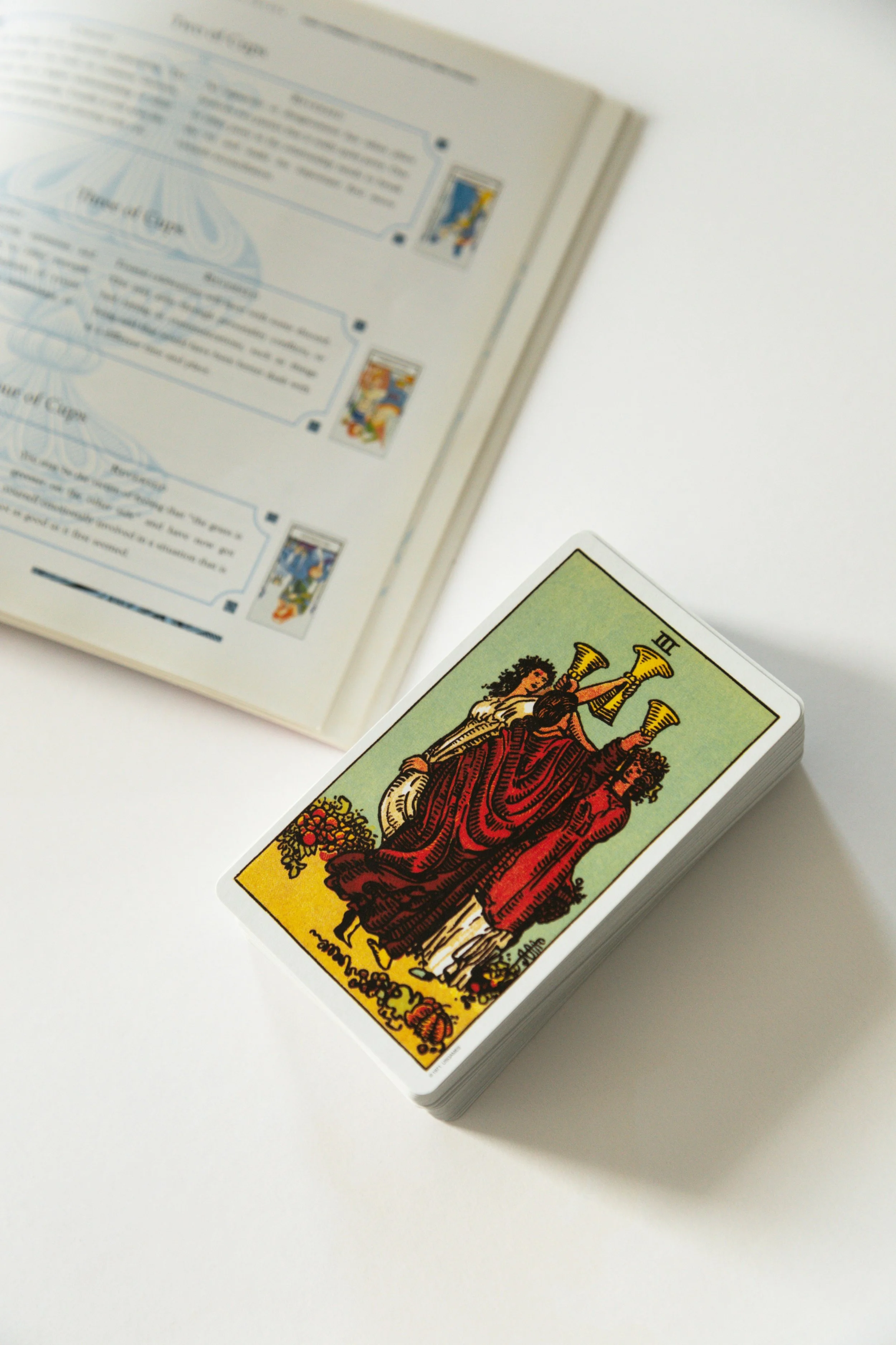 Top of a tarot card deck with the Tower card showing, partially covering a book or manual on tarot reading.