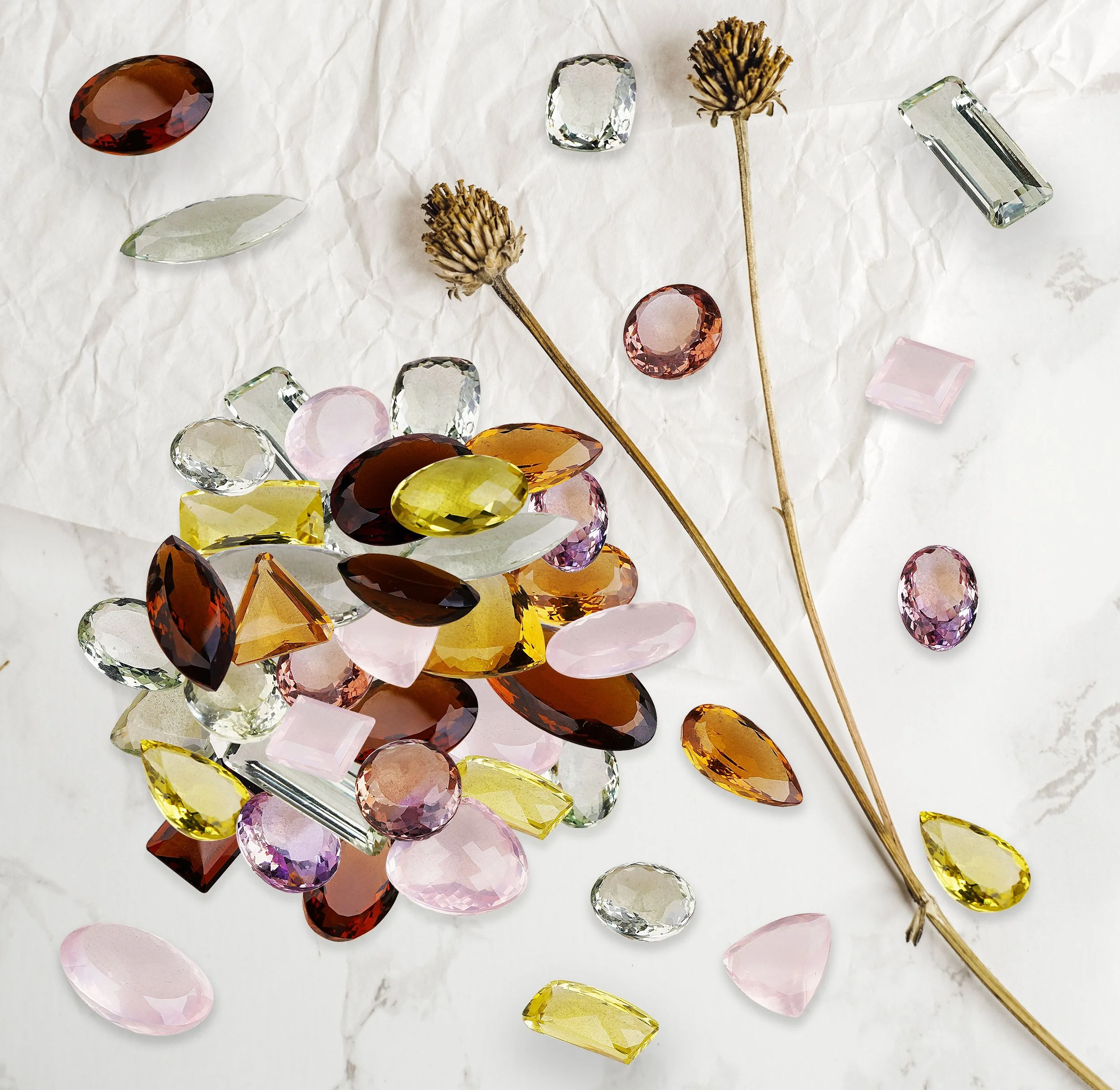 Assorted colorful gemstones and dried flowers scattered on white crumpled paper background.