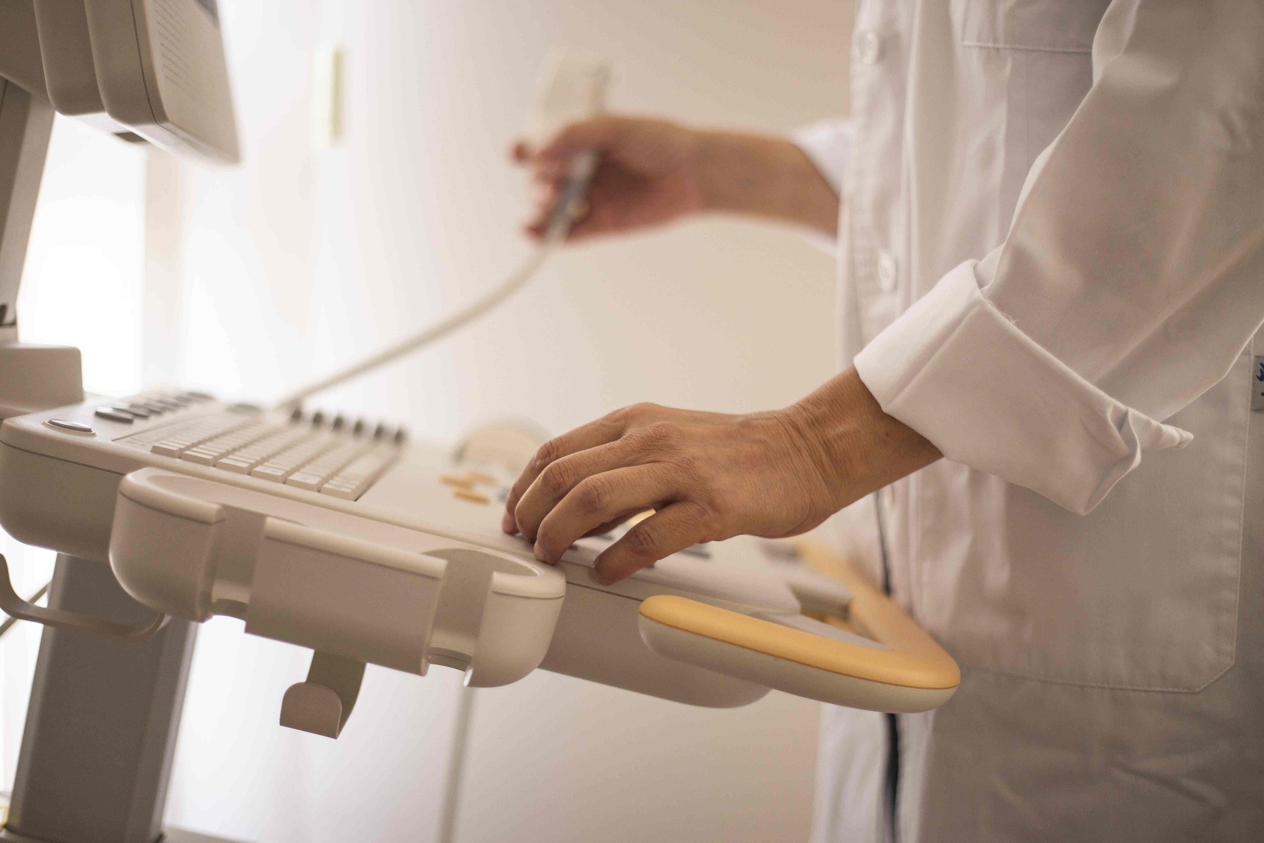 A close-up of a person's hands typing on a computer keyboard, with a medical or laboratory setting in the background.