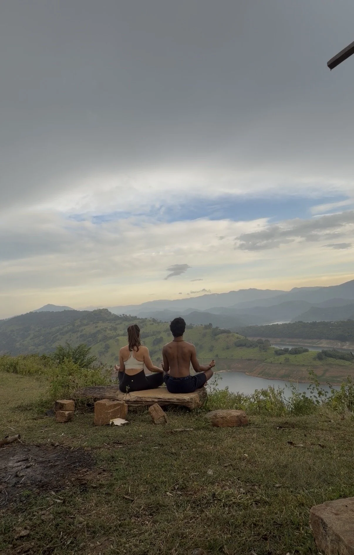 Two people practising yoga and meditation outdoors in Sri Lanka, overlooking the mountains and Victoria Lake.