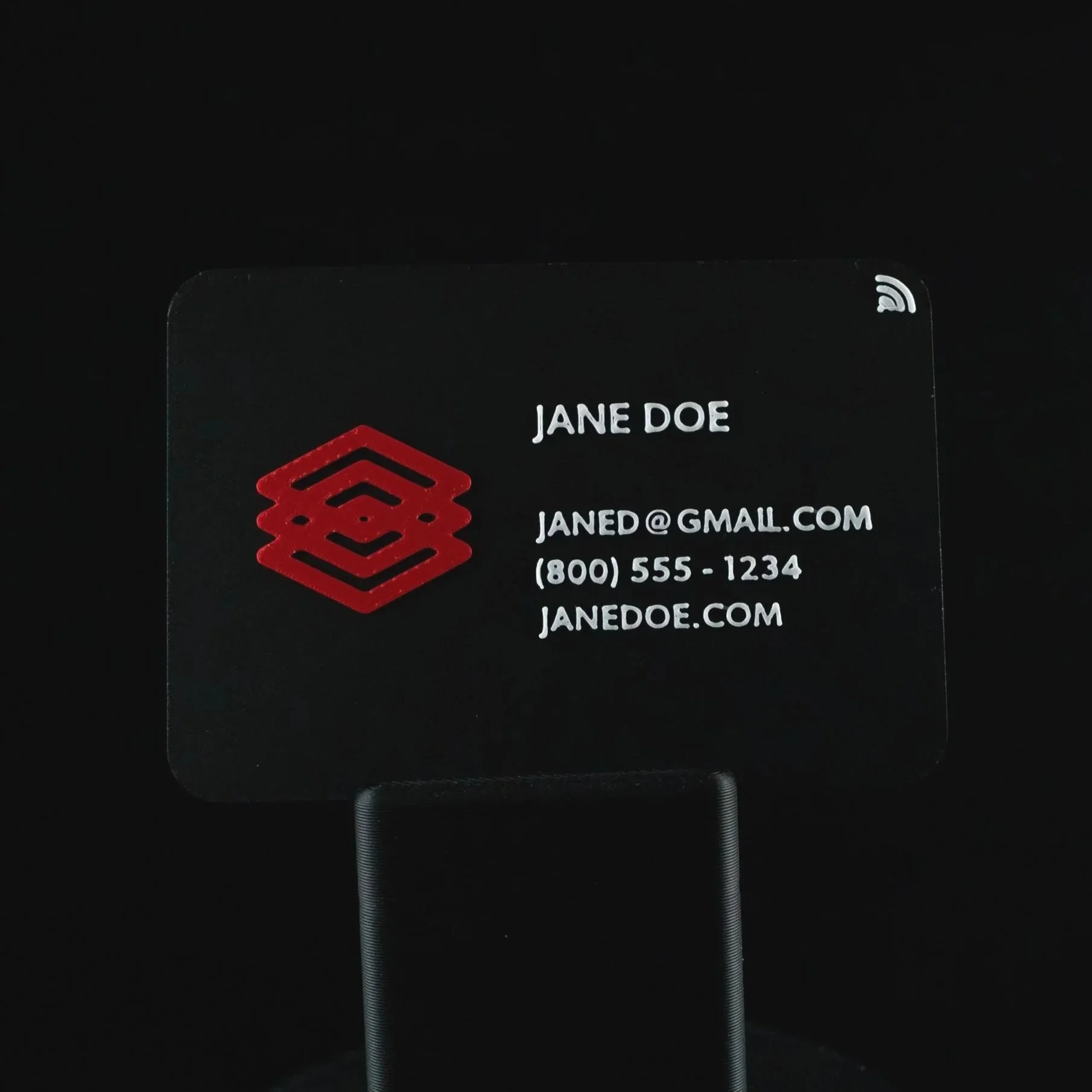 Close-up of a Black 3D-printed NFC business card with red and white text and a red geometric logo, showing an email address and phone number.