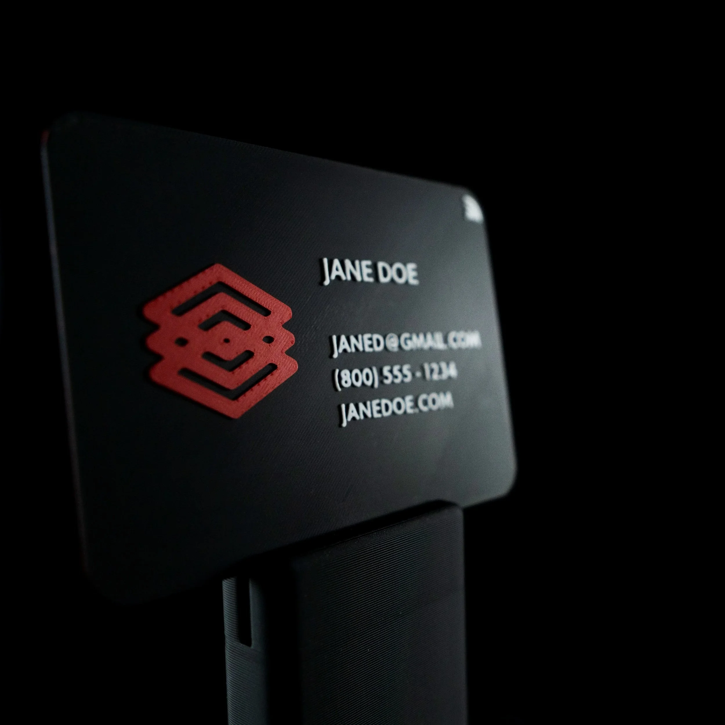 Close-up of a 3d printed business card with a red symbol, set against a dark background.