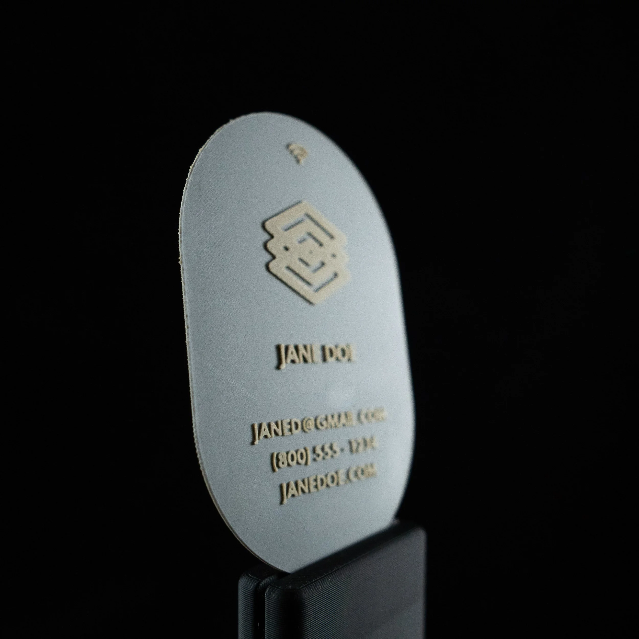 Close-up of a oval shaped 3D printed business card in a grey and tan color scheme. 