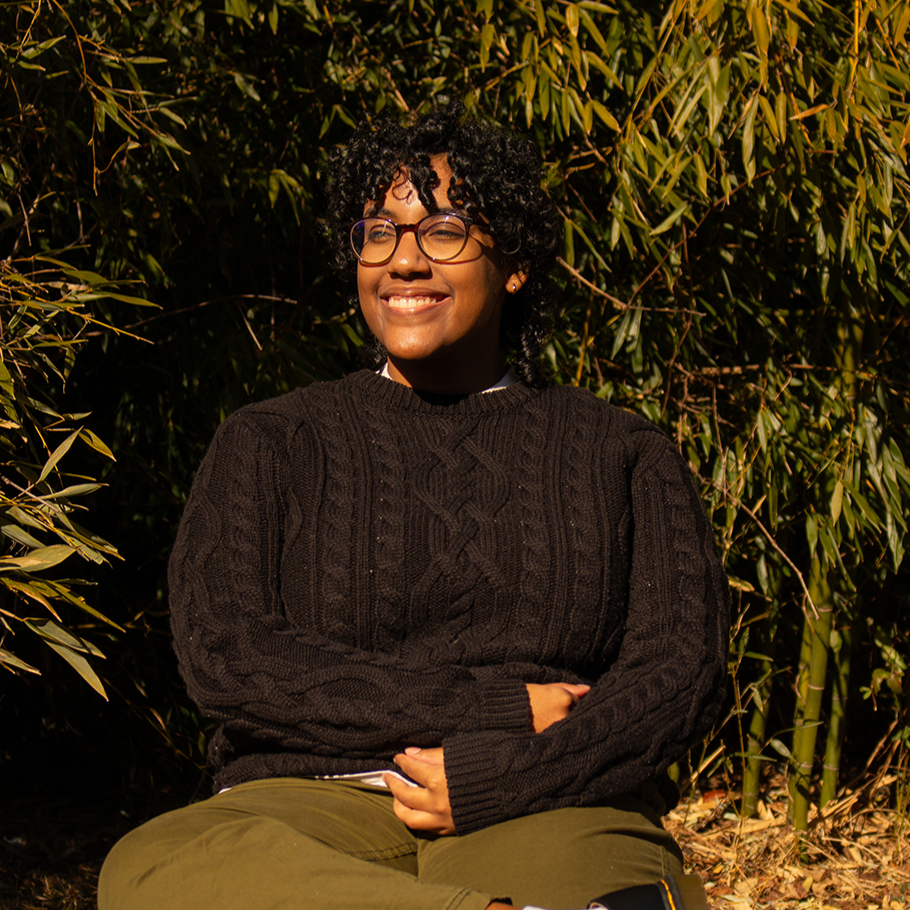 Co-founder Kayley with curly black hair and glasses sitting outdoors and smiling.