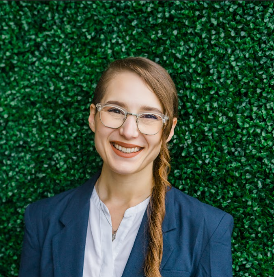 Co-founder Victoria with glasses and a braid smiling in front of a green leafy background.