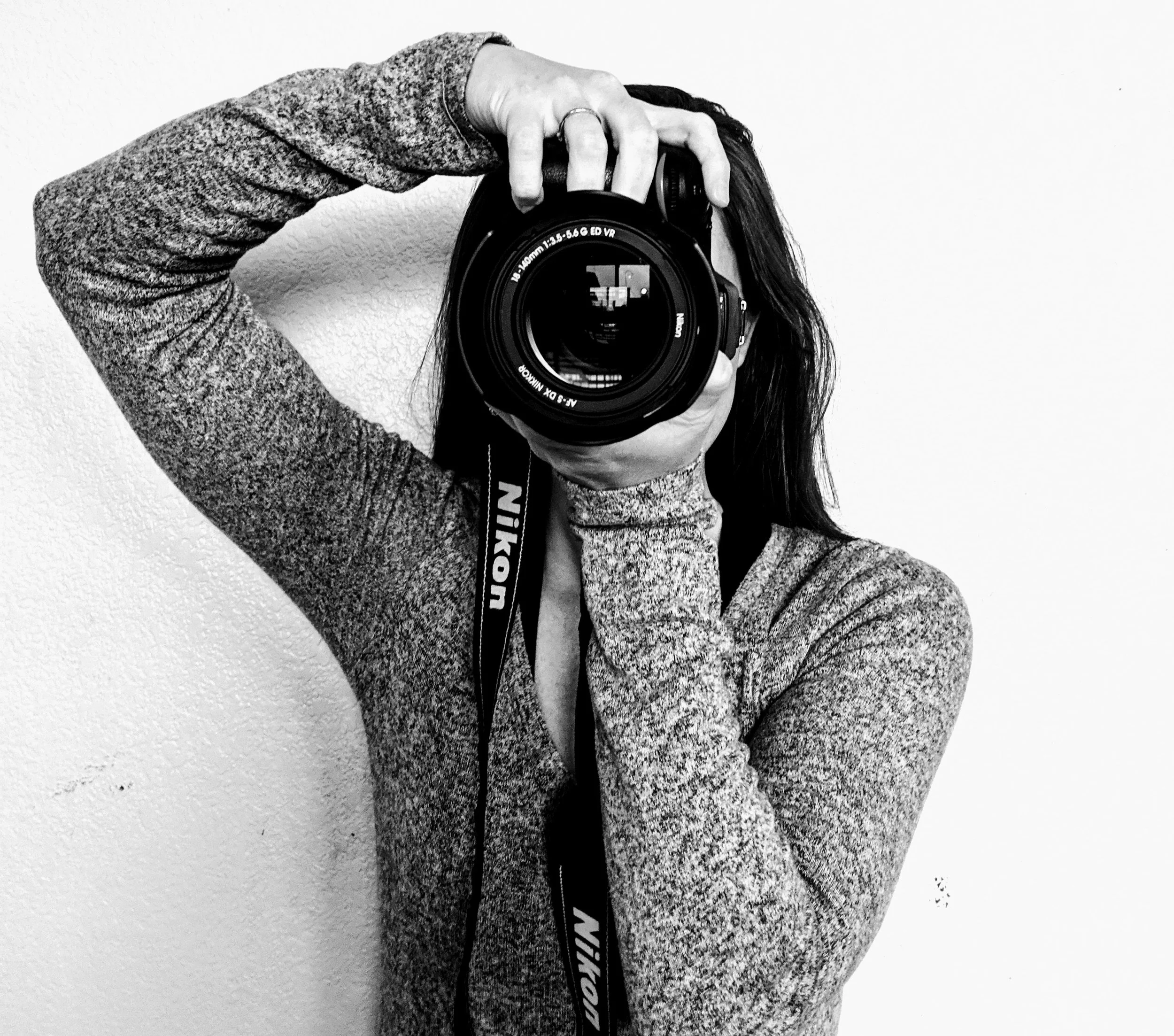 Person taking a mirror selfie with a camera, wearing a textured hoodie, with long hair partially covering their face.