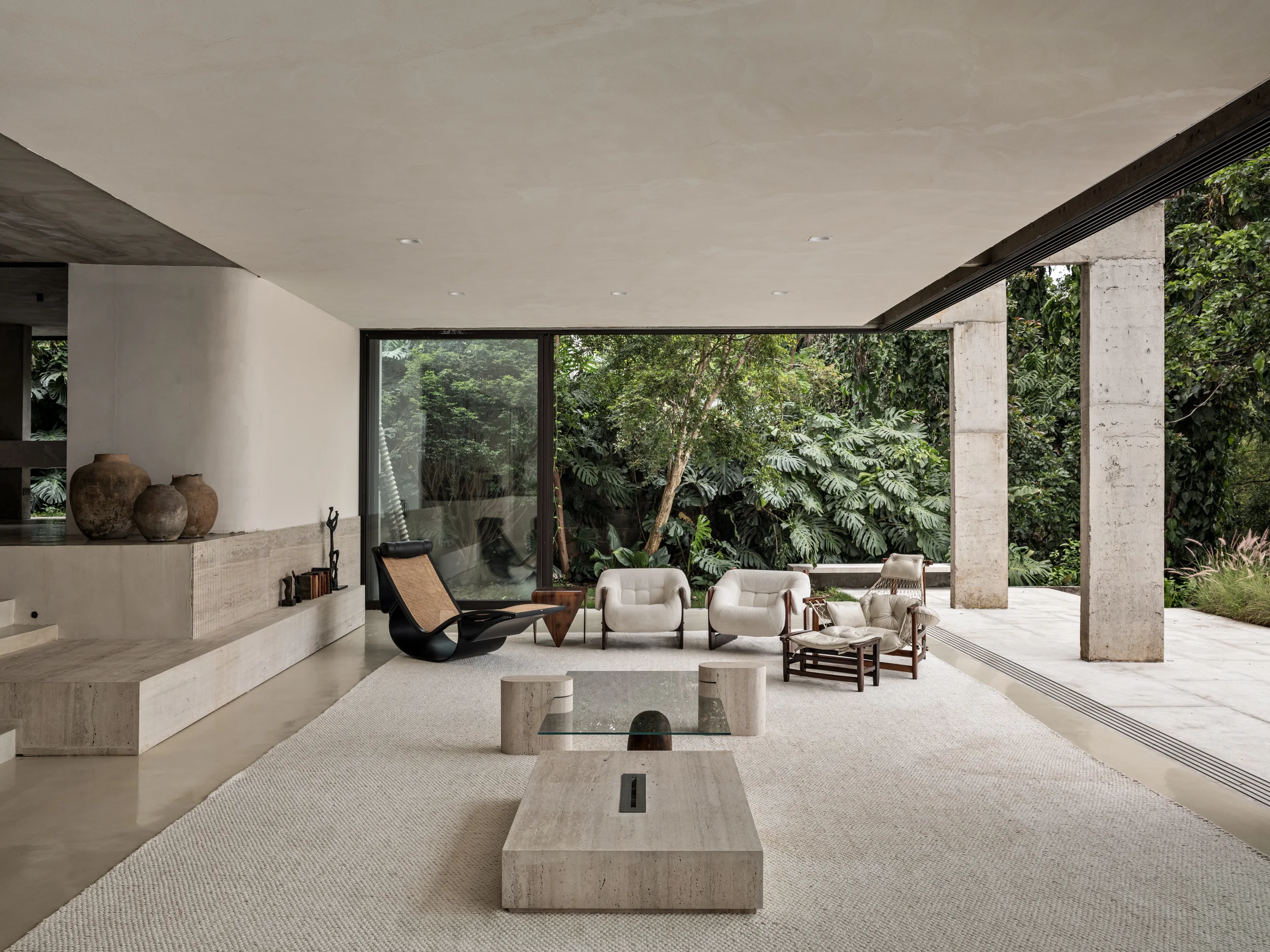 Sala de estar da Casa dos Pessegueiros, projeto do Estudio Sala, com pilares de concreto aparente, mobiliário contemporâneo e grandes aberturas para a vegetação.