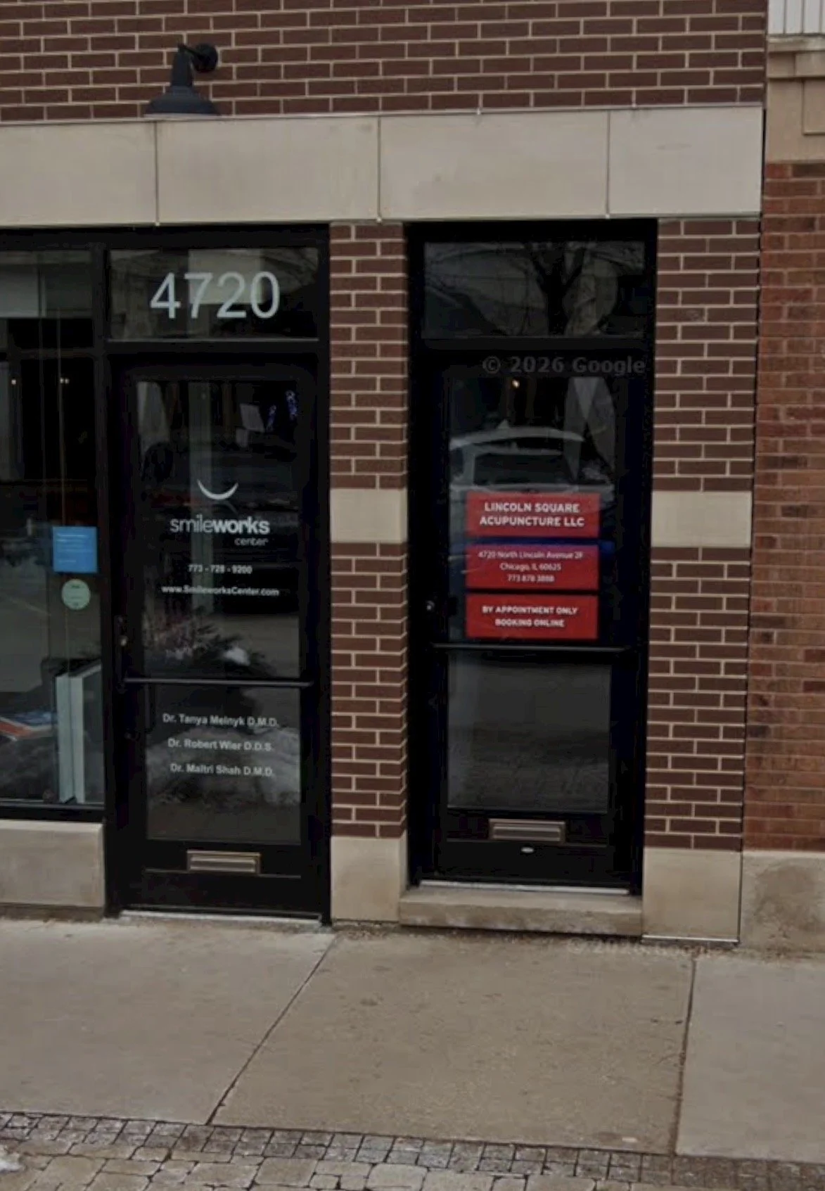 The street view of the clinic entrance, which is to the right of SmileWorks dentistry. The clinic door has a red sign that says "Lincoln Square Acupuncture", as Liberation Acu shares space with them. The door is a half step up from the sidewalk.