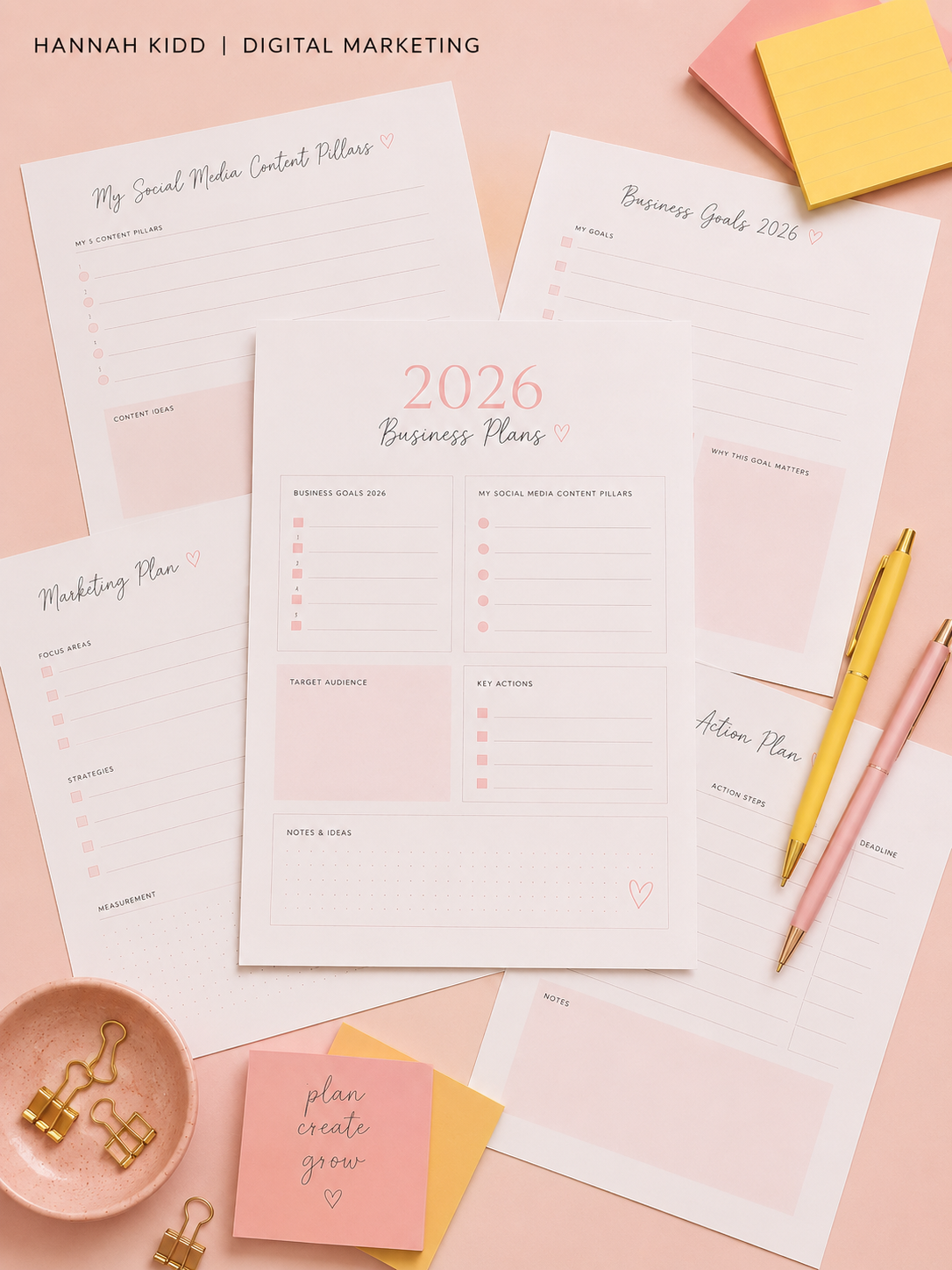 Various 2026 business planning and social media content creation sheets in pink and white with pens, sticky notes, and gold paper clips on a pink background.
