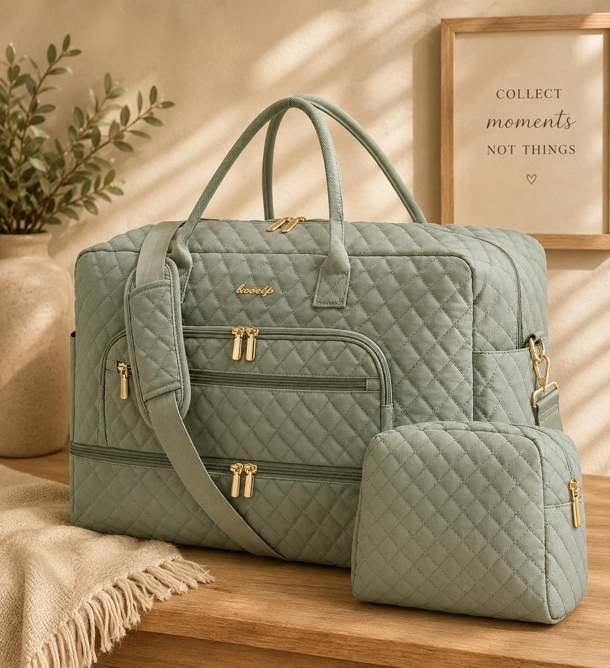 A green quilted travel bag with multiple zippered compartments, a matching smaller bag, and a detachable shoulder strap, on a wooden surface with a beige blanket, a plant in a pot, and a framed sign that says 'Collect moments not things.'