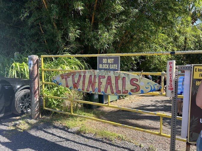 Entrance gate to Twin Falls park with a colorful sign, yellow gate, and trees in the background.